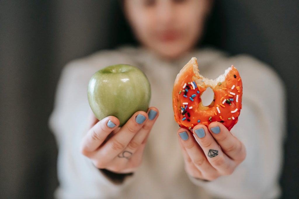 woman showing apple and bitten doughnut