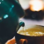 person pouring liquid into brown ceramic cup