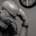 grayscale photo of man thinking in front of analog wall clock