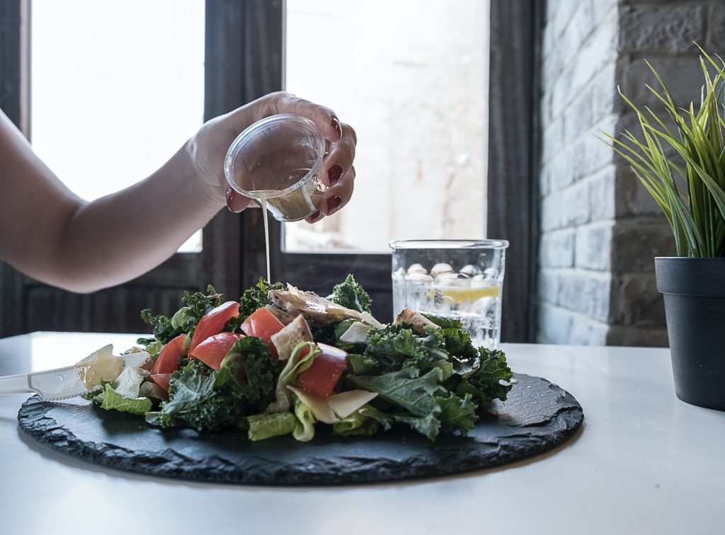 person pouring dip on vegetable salad