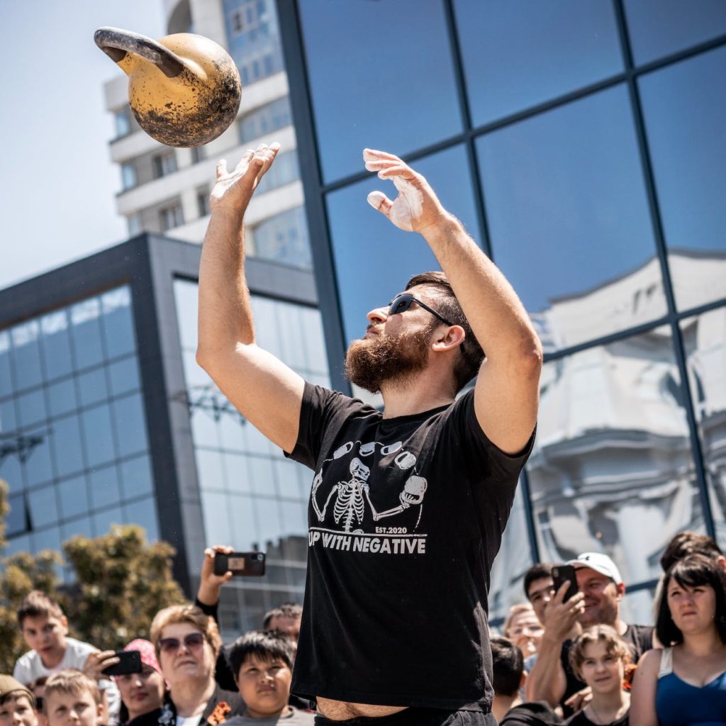 man throwing a metal ball in a city center and crowd watching