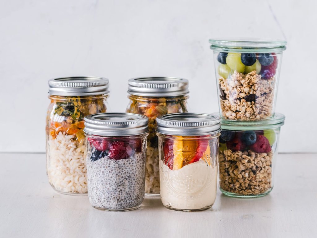 six fruit cereals in clear glass mason jars on white surface