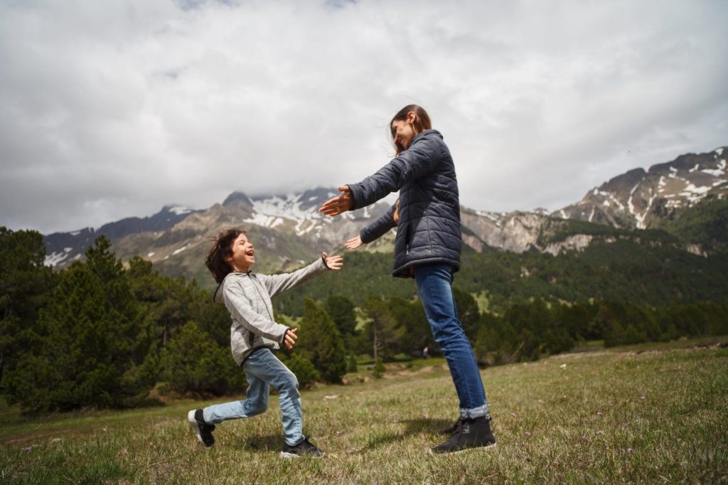 woman and child playing on green grass field near mountain