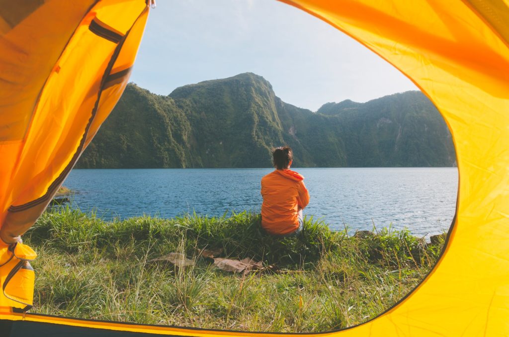 person sitting on grass field facing on body of water