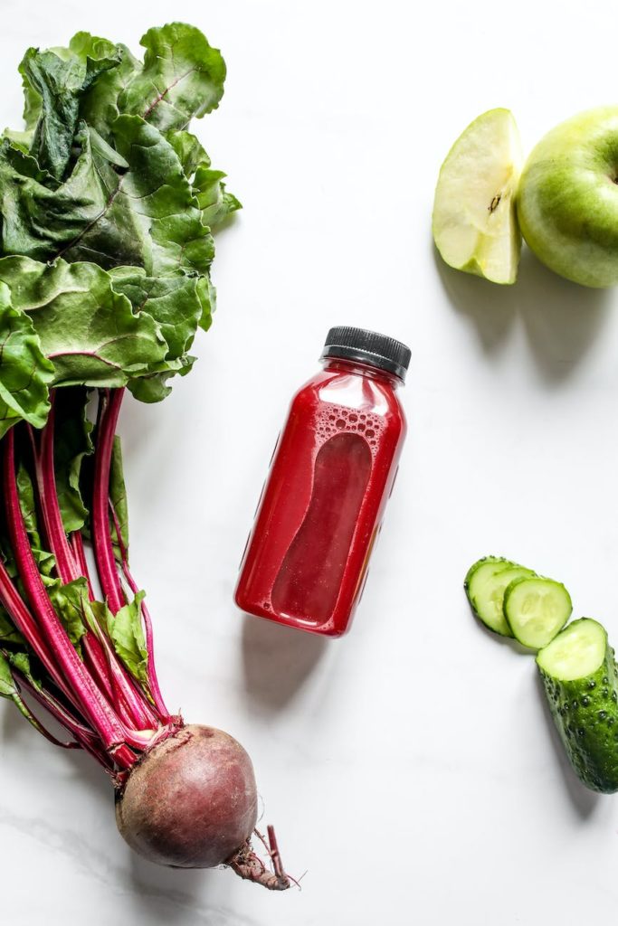 red juice in bottle beside beetroot apple and sliced cucumber