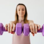 purple dumbbells in hands of positive sportswoman