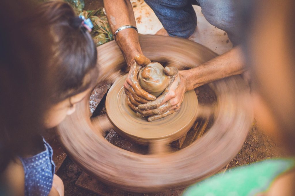 person making clay pot in front of girl during daytime