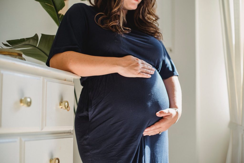 crop pregnant woman embracing tummy in room at home