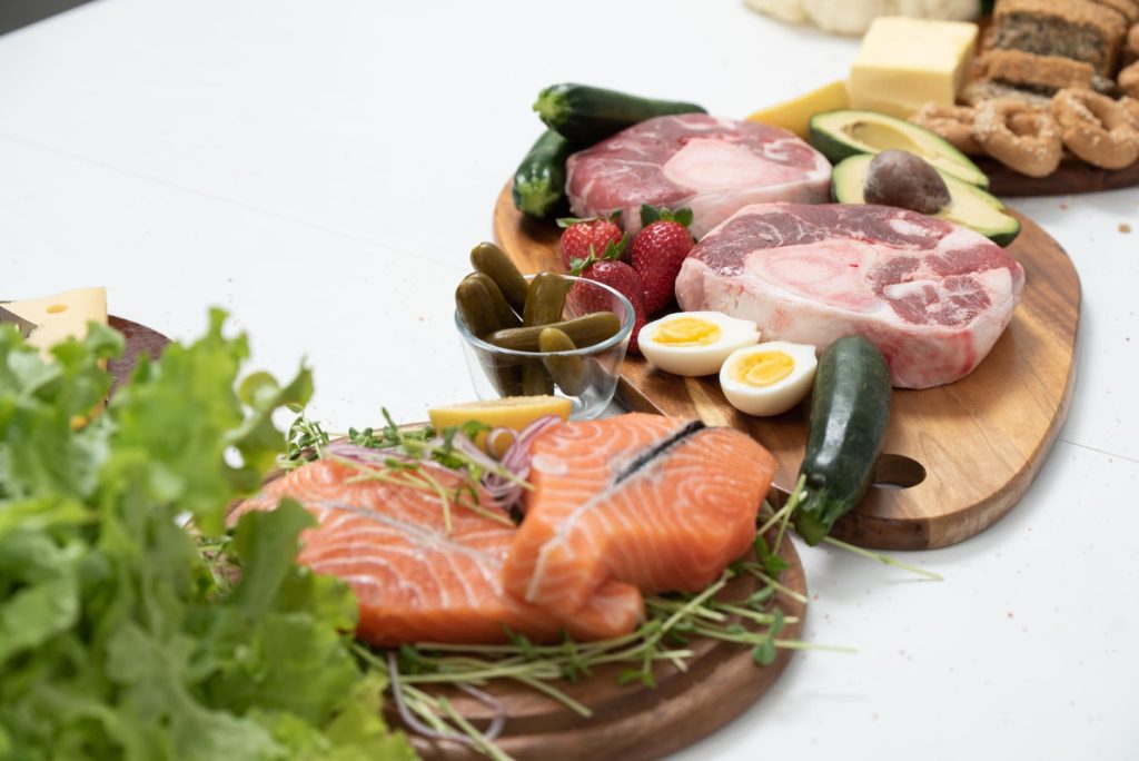 assorted fresh meat and salmon with fruits and vegetables on a chopping board