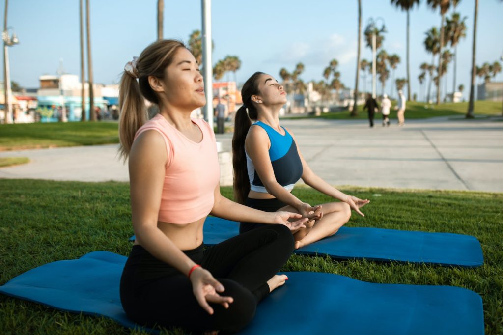 women meditating in the park with yoga mats