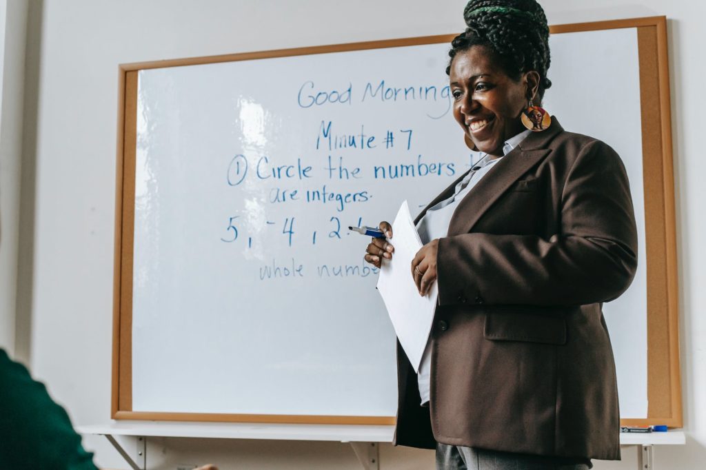 crop cheerful black female teacher standing near whiteboard in classroom