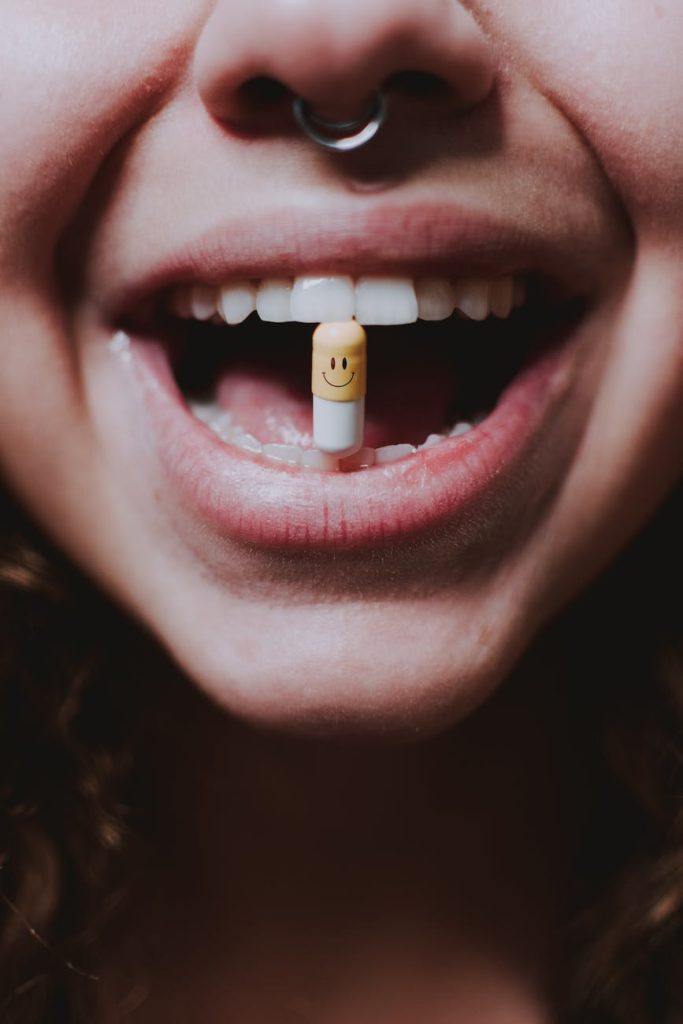 faceless woman with pill in teeth and nose piercing