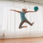 slim woman in sportswear jumping up with ball