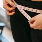 plus size woman measuring hips in gym