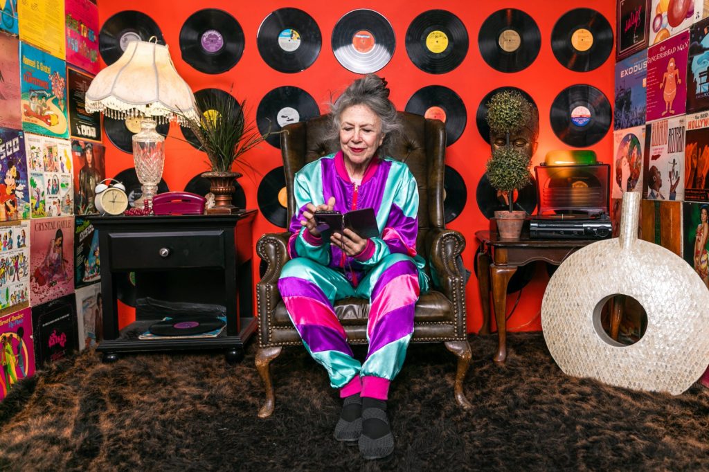 elderly woman in purple and pink outfit sitting on brown leather armchair