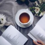 white ceramic teacup with saucer near two books above gray floral textile