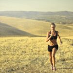 cheerful sportswoman running along hill in summer