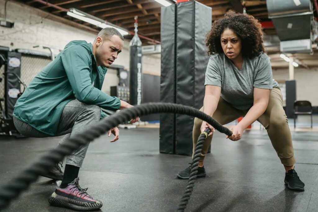 focused black woman exercising with battling ropes near coach