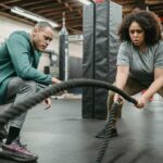 focused black woman exercising with battling ropes near coach